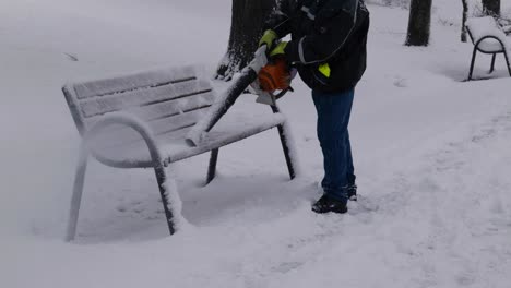Man-Removing-Snow-From-Public-Park-Bench-With-Leaf-Blower