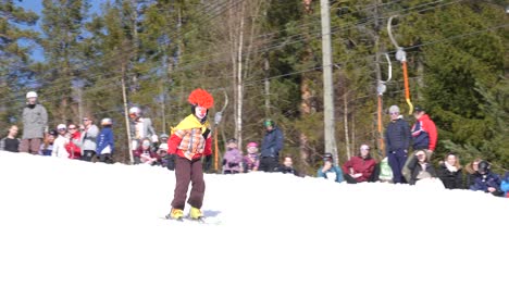 Teen-dressed-as-a-clown-skis-down-a-snow-hill-and-splashes-across-a-pool-of-water-at-a-community-event