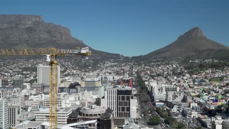 A-tower-crane-operates-at-city-high-rise-construction-site-with-Table-Mountain-and-Lion's-Head-as-backdrop-in-business-district-of-Cape-Town