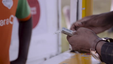 Hands-of-a-mobile-money-customer-counting-out-cash-money-notes-and-handing-over-to-the-mobile-money-agent-at-a-kiosk