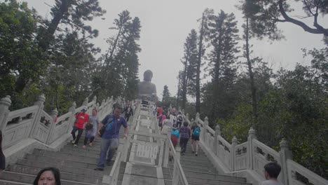 Tian-Tan-Buddha-Im-Dorf-Ngong-Ping-An-Einem-Bewölkten-Tag-Mit-Vielen-Touristen-Und-Besuchern,-Die-Die-Treppen-Hoch-Und-Runter-Laufen-–-Rotierende-Handkamera