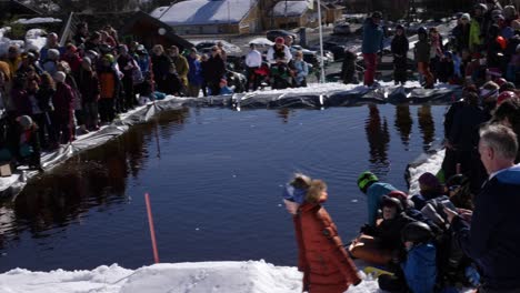 Crowd-at-a-community-event-where-people-ski-down-a-hill-and-try-to-get-across-a-pool-at-the-bottom