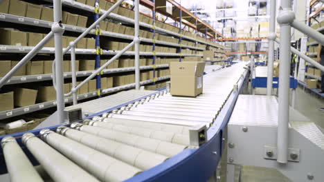 Pan-shot-follows-packing-box-around-corner-of-roller-conveyor-as-it-travels-past-stock-shelves-in-large-automated-warehouse-distribution-center