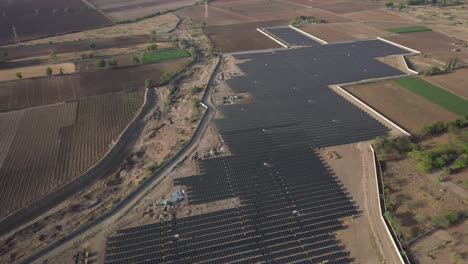 Aerial-wide-angle-view-where-a-big-solar-power-plant-is-visible-and-there-are-many-fields-around