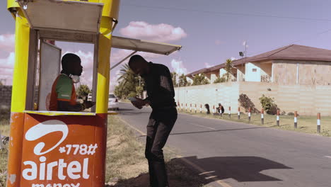 A-male-customer-arriving-at-a-mobile-money-kiosk-and-greeting-the-agent-with-a-fist-pump-in-Lusaka,-Zambia