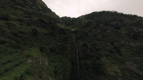 FPV-drone-flying-towards-a-waterfall-in-lush-green-rugged-terrain-forest-in-Madeira