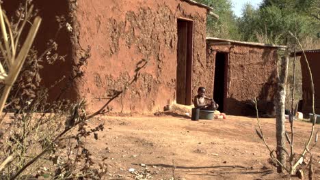 A-young-African-boy-uses-a-plastic-tub-to-bathe-outside-his-traditional-mud-house