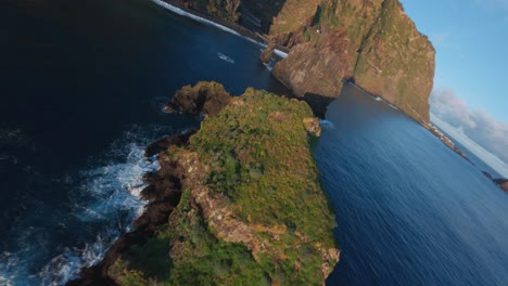FPV-drone-flying-over-the-blue-ocean-between-rock-formations-at-the-coast-of-Ribeira-da-Janela,-Madeira-at-sunrise
