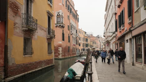 Walking-People-On-Typical-Street-By-Canal,-Boats-Moored,-Winter,-Venice