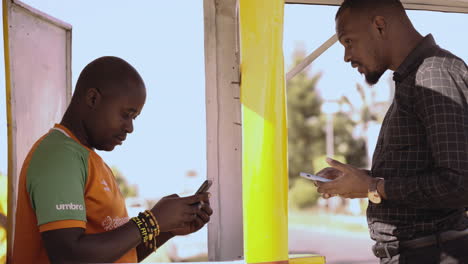 A-mobile-money-agent-and-customer-use-their-handheld-smartphones-to-transact-at-a-money-kiosk-in-Lusaka,-Zambia