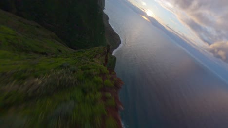 FPV-drone-diving-down-to-the-ocean-from-a-mountain-proximity-at-a-ridgeline-where-lush-green-nature-is-visible