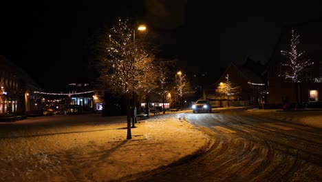 Kleine-Stadt-In-Der-Nacht,-Dekoriert-Für-Weihnachten-Und-Neujahr,-Während-Ein-Auto-Im-Schnee-Vorbeifährt