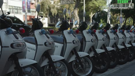 Row-of-white-police-motor-scooters-lined-up-on-a-city-street,-daytime,-urban-transportation-theme