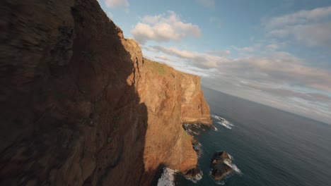 FPV-drone-flying-close-to-the-edge-of-the-cliff-at-sunrise-over-the-ocean-at-Madeira-Ponta-Do-Rosto