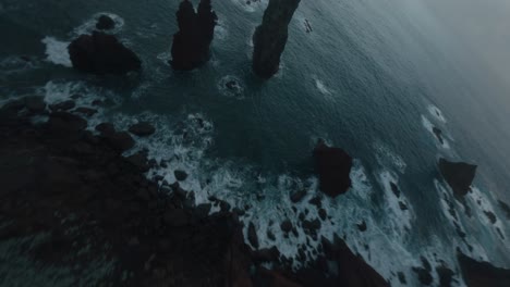 Cinematic-FPV-drone-flying-over-the-edge-of-a-cliff-diving-down-to-the-ocean-where-waves-collide-with-the-sharp-cliffs-of-a-rugged-coastline-under-the-soft-light