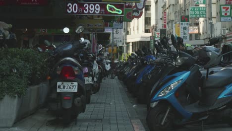 Row-of-parked-scooters-lining-a-busy-street-in-Zhongshan,-Taipei-during-daytime,-city-life