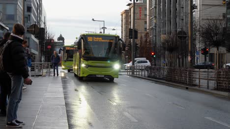 Commuters-wait-for-a-bus-at-a-stop-in-the-Barcode-area-of-Oslo,-Norway-on-a-cold,-wet-winter's-day