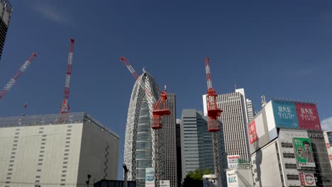 Construction-cranes-stand-against-the-backdrop-of-the-building-skyline-in-proximity-to-Shinjuku-Station,-Japan
