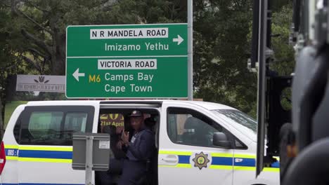 Police-officer-in-police-vehicle-parked-beneath-Cape-Town,-Mandela-road,-Imizamo-Yethu-signpost