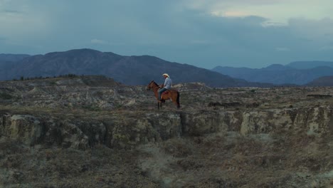 Majestätischer-Cowboy-Zu-Pferd-Auf-Dem-Bergrücken-Der-Wüste-Bei-Sonnenuntergang,-Luftaufnahme