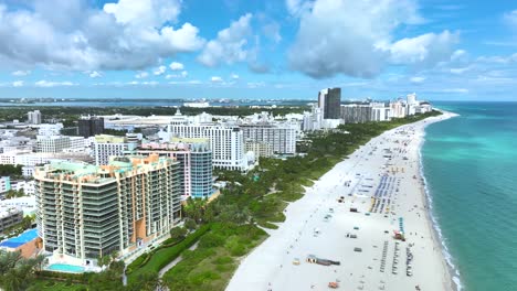 Magnificent-aerial-drone-footage-of-a-sandy-beach-in-Miami,-USA,-slow-forward-movement-revealing-a-beautiful-seascape,-with-people-relaxing,-and-tall-buildings