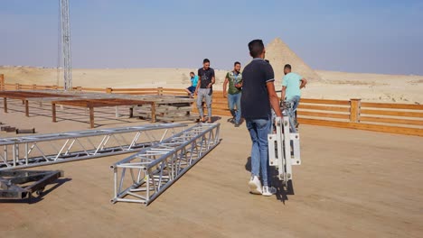 people-prepare-the-stage-for-a-party-in-the-desert-beside-the-Pyramids,-Giza-in-Egypt,-static-shot