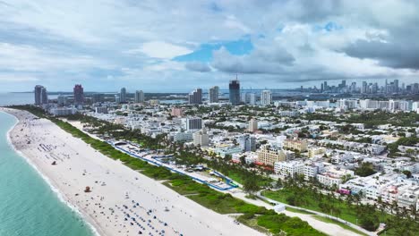 Spectacular-aerial-drone-footage-of-a-sandy-beach-in-Miami,-USA,-slow-rising-pedestal-shot-capturing-a-fascinating-seascape,-with-people-relaxing,-and-tall-buildings