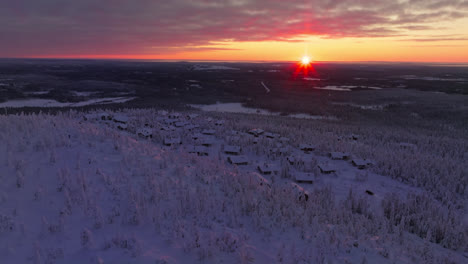Panoramic-drone-shot-orbiting-snowy-cottages-on-the-Iso-Syote-fell,-sunset-in-Finland