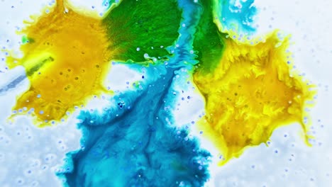 Bright-yellow-and-blue-ink-drops-in-water-with-a-bubbling-effect,-high-angle-shot