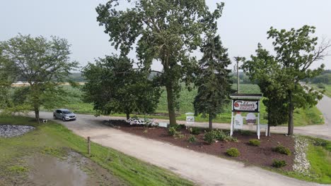 Car-leaving-Calder-Dairy-Farm,-aerial-view-of-entrance-with-logo-board