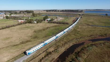 long-passenger-train-traveling-through-countryside,-blue-and-white-cars,-near-Buenos-Aires