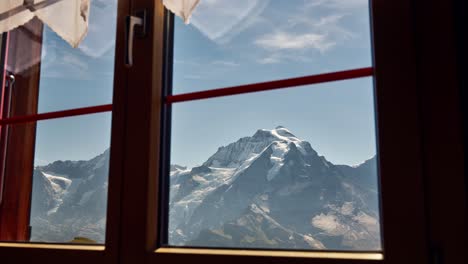 Vista-De-La-Escarpada-Cresta-Alpina-Con-Nieve-Desde-El-Interior-De-La-Casa-Del-Complejo-De-Montaña,-Vista-Desde-La-Ventana