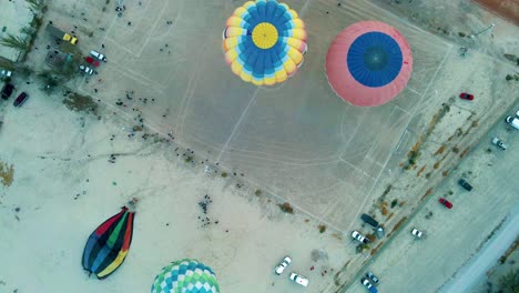 Aerial-panning-shot-flying-over-colorful-hot-air-balloons-inflating-and-preparing-to-take-off-during-ballooning-festival