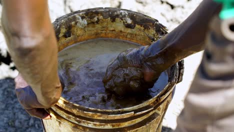 Male-Hands-Preparing-Mud-In-Bucket-For-Termite-Mounds-In-Animal-Waterhole-In-Uganda