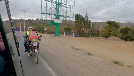 Motorcycle-Driving-Next-To-Four-wheeled-Vehicle-On-Asphalt-Road-In-Narok,-Kenya
