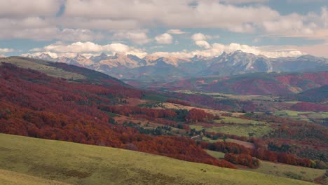 timelapse-view-of-Snowy-mountain-peaks,-orange-and-green-forest-in-fall-autumn-season-on-a-sunny-and-cloudy-day