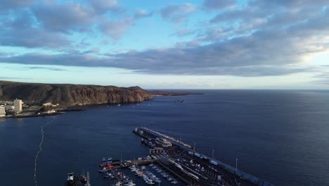Aerial-over-port-of-Los-Cristianos,-calm-sea,-sun-reflexion-at-sunset,-Canary-Islands-Tenerife