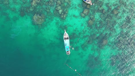 Longtail-boat-moored-at-reef-in-turquoise-clear-water,-Aerial-top-down