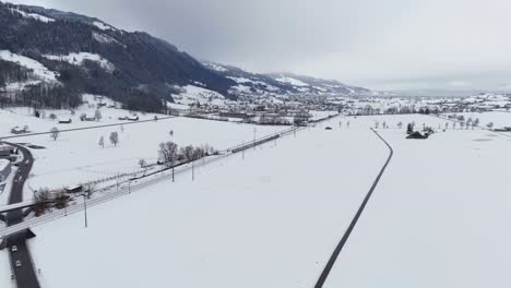 Drohnenaufnahme-Zeigt-Bewölkten-Tag-In-Der-Wintersaison,-Mit-Kleinem-Dorf-Und-Schneebedeckten-Feldern-In-Der-Schweiz