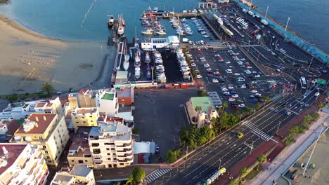 Busy-cargo-port-near-seaside-beach-in-Los-Cristianos-Tenerife,-aerial-establish-shot,-Canary-islands