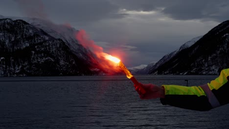 Ship-crew-member-holding-emergency-flare,-background-of-winter-fjord-at-night