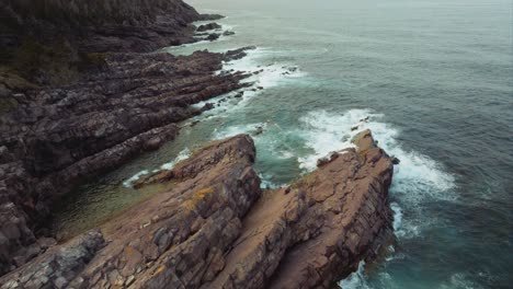 Drone-flying-low-over-rocky-coast-with-waves-smashing-against-the-shore
