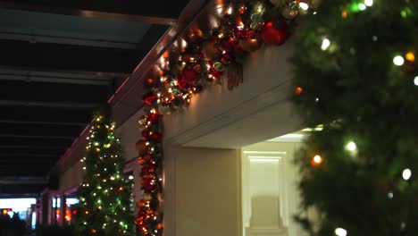 Mittlere-Aufnahme-Eines-Weihnachtskugelkranzes,-Der-über-Dem-Eingang-Eines-Luxushotels-Hängt-Und-Aus-Roten-Und-Goldenen-Kugeln-Sowie-Lichterketten-Mit-Einer-Grünen-Pflanze-Im-Vordergrund-Besteht