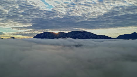 El-Sol-Naciente-Brilla-Sobre-Los-Picos-De-Las-Montañas,-Que-Están-Envueltos-En-Nubes