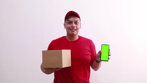 Young-asian-deliveryman-holding-cardboard-while-showing-green-screen-mobile-phone-display
