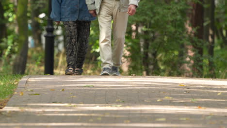 Two-people-walking-together-on-a-park-path-holding-hands,-close-up-on-walking-feet,-daytime,-intimate