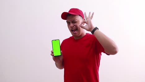 Young-handsome-asian-deliveryman-showing-green-screen-phone-display-and-making-okay-hand-gesture