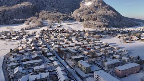 Whole-village-covered-with-snow-beside-the-mountain-during-winter-season,-aerial-dynamic