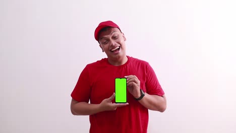 Fröhlicher-Junger-Asiatischer-Kurier-In-Rot-Steht,-Während-Er-Ein-Leeres-Handy-Display-Mit-Grünem-Bildschirm-Zeigt