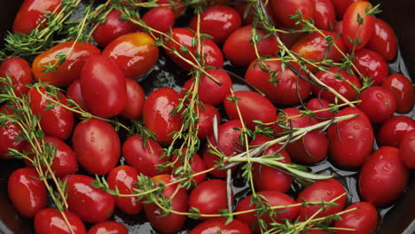 Vibrantes-Tomates-Cherry-En-Una-Sartén-Rústica-De-Hierro-Fundido,-Cubiertos-Con-Romero-Y-Tomillo,-Listos-Para-El-Horno